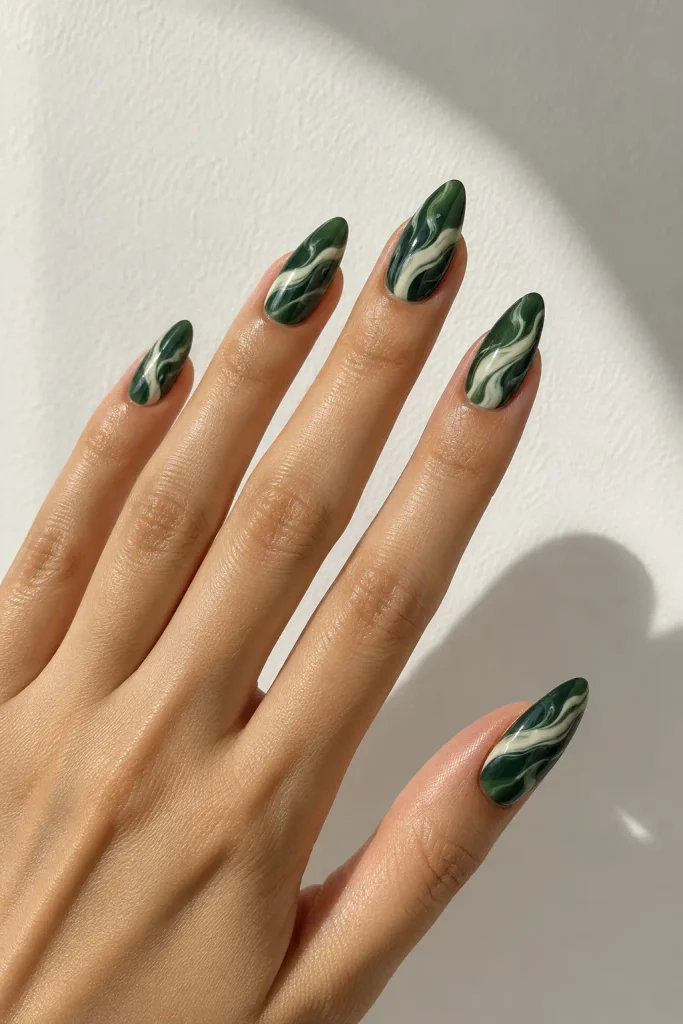 Dark green nails featuring elegant swirling cream marble patterns