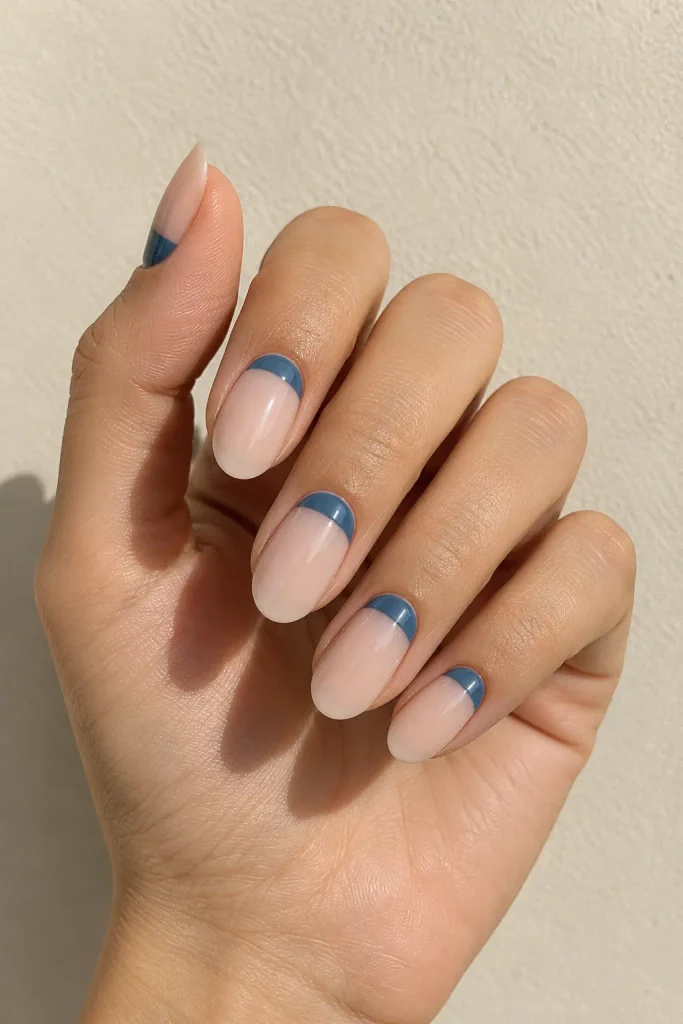 Nude almond nails with curved blue half-moon accents near the cuticles.