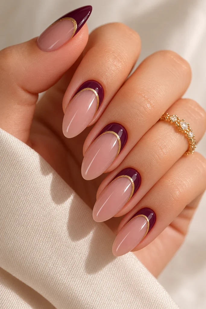 Plum reverse French crescents outlined with thin gold lines on almond nails.