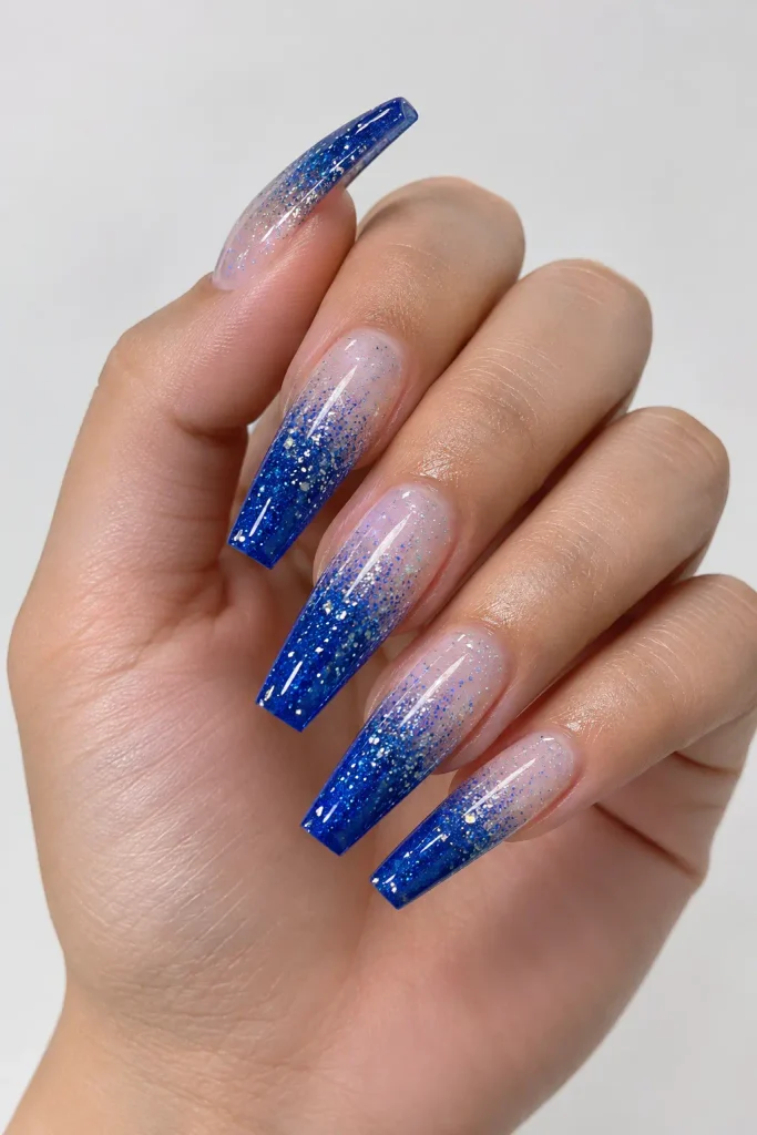 Long coffin nails fading from a sheer base to sparkling sapphire blue tips.